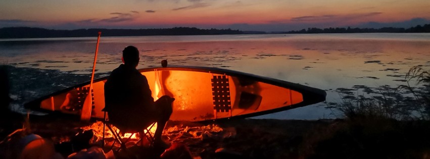 Me sitting by a canoe tending a fire